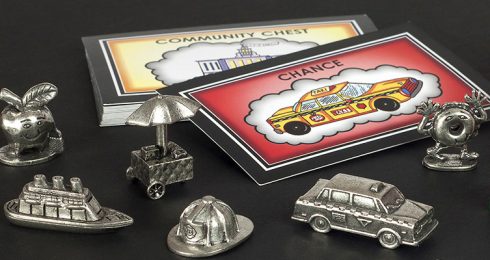 New York Edition of Monopoly pieces, including a dancing bagel, apple, Staten Island ferry, hot dog cart, NYFD helmet, and NY taxi cab