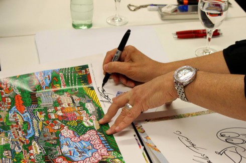 Close up image of Charles Fazzino's hands signing a piece of artwork