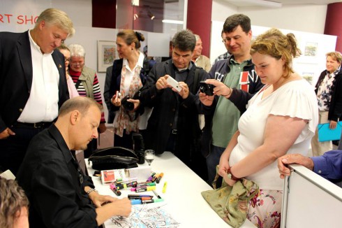 Fazzino surrounded by crowds of fans as he signs a piece of artwork for a young women.