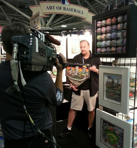 Fazzino standing in front of a video camera ready to be interviewed as he holds up his hand painted home plate.