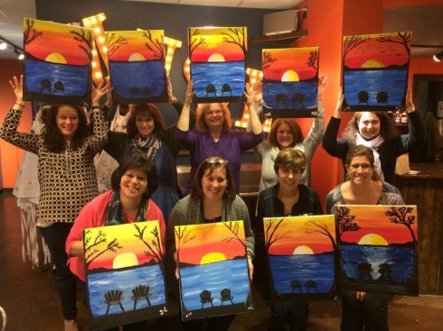 A group of people gather to show off their artwork created at a Paint Party