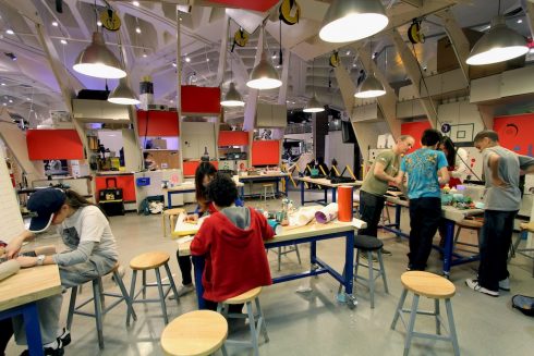 Children and teens gathered around tables creating and building things inside a makerspace.