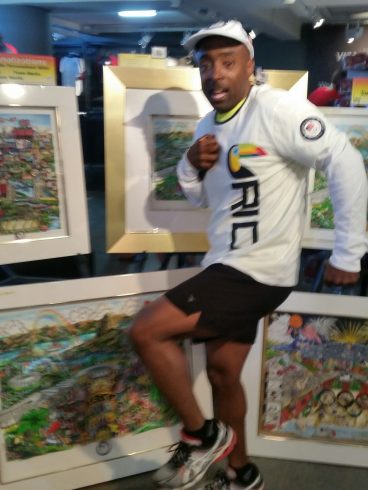 A man in a white long sleeved shirt and black shorts posing in front of the Fazzino's 2016 Olympic Games collection.