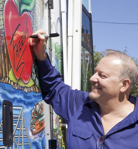 Charles Fazzino signing a read pop-art apple on the side of the Westchester Medical Center Health Center custom wrapped bus