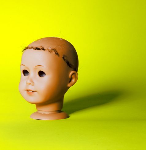 A photo of a doll head with a neon yellow background shot by photographer Nicholas Rouke