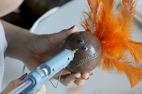 Using a glue gun to attached blue googly eyes to a baseball