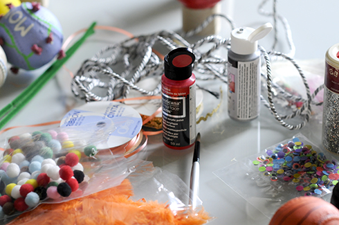 A table full of craft supplies like pom poms, paint, brushes, ribbons for making baseball art