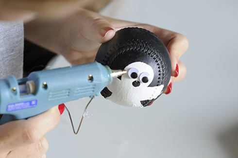 Using a heat gun to attach googly eyes for a ghost painted on a baseball