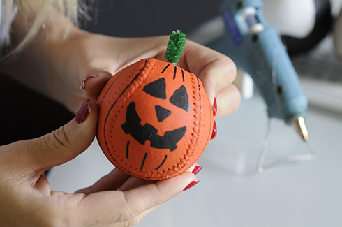 A pumpkin baseball with triangle eyes, teeth and a pipe cleaner stem