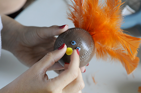 Adhering a pom pom as a nose to a baseball turkey art