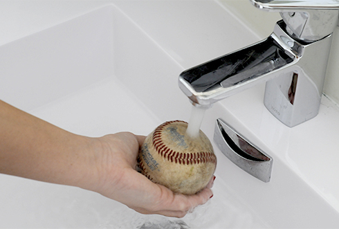 Holding a baseball under the water to clean in it preparation for arts and crafts