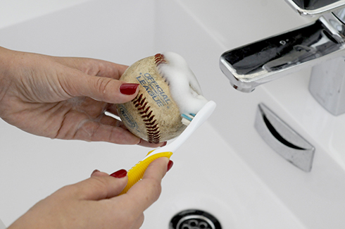 Scrubbing a baseball with a toothbrush to clean it up for art projects