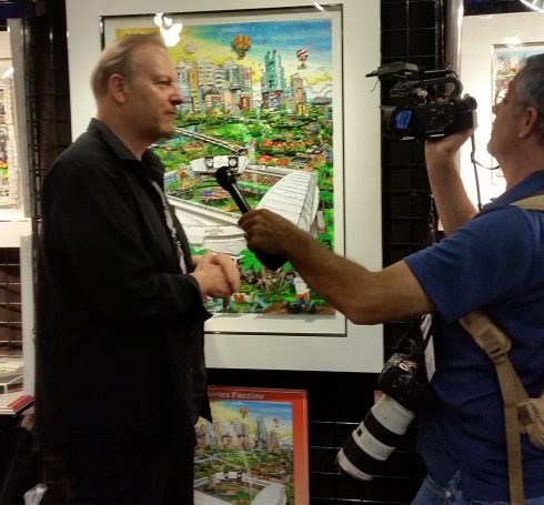 Charles Fazzino standing in front of his 2017 All-Star 3D pop art collection, being interviewed at MLB Fan Fest 