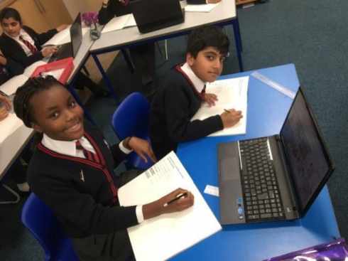 Two kids looking up from doing research on their laptop at the Primary School in the UK