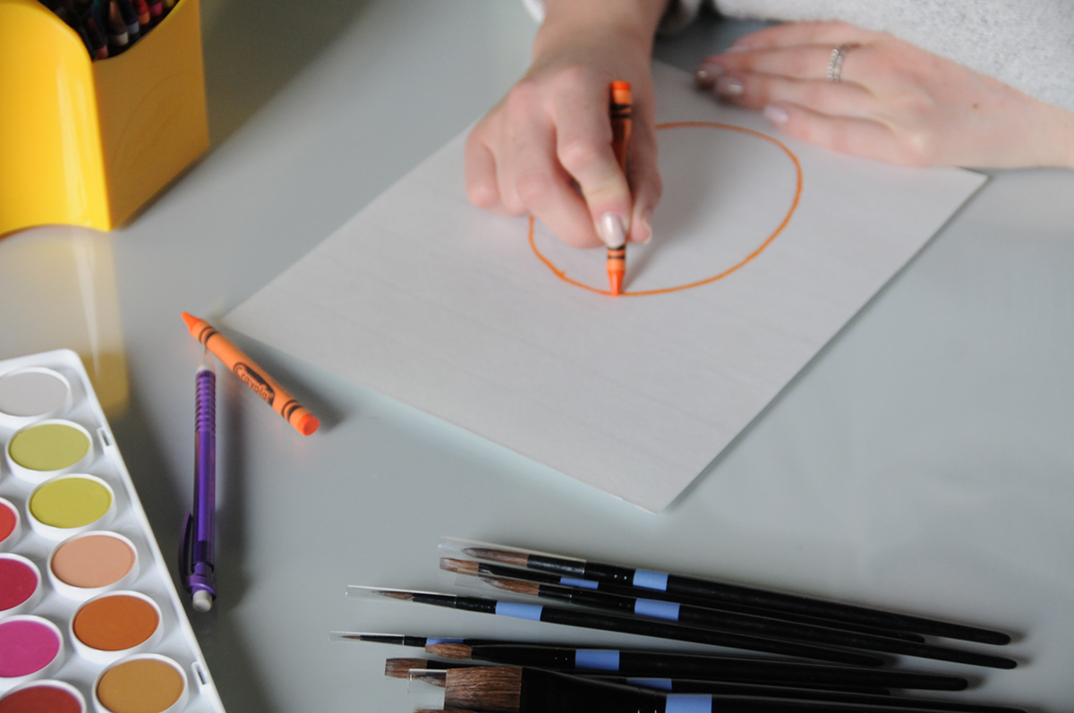 An orange circle in the shape of a pineapple being drawn on watercolor paper