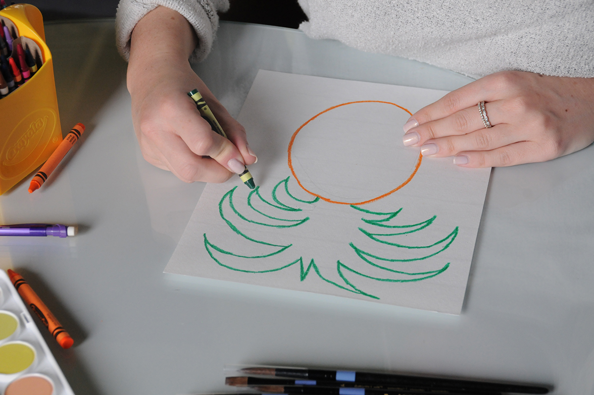 Using a green crayon to draw the leaves of a pineapple