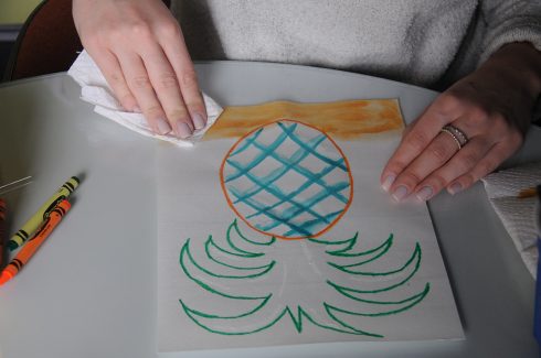 Using a paper towel to remove watercolor from a pineapple painting for a reductive effect