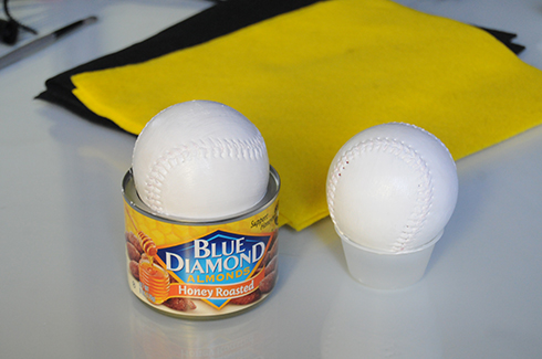 Two baseballs painted white sitting on top of a nuts can and dressing cup to dry