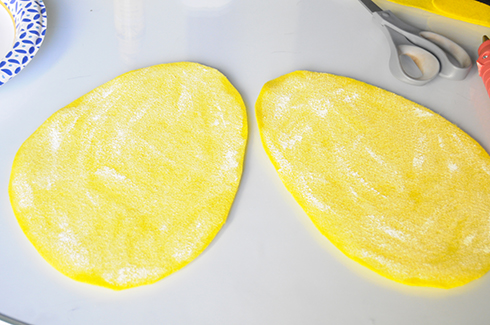 Two pieces of yellow felt shaped like bee wings with white paint lightly brushed on the surface