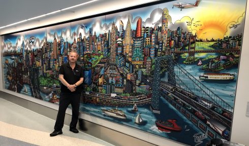 Charles Fazzino standing in front of a 3D pop art mural of a New York City skyline in NYU Langone Health