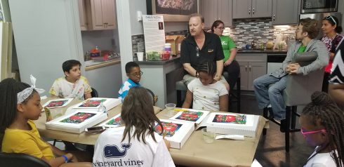 Charles Fazzino sitting on a stool in the Fazzino Art Studio kitchen talking to "It Takes a Village to Educate a Child" students before they start their art project.