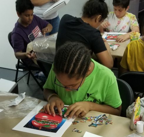 "It Takes a Village to Educate a Child" student wearing glasses and a green t-shirt working on a Charles Fazzino 3D Pop Art project at his studio in New Rochelle