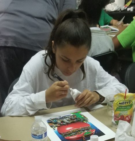 A young girl with brown hair pulled back in a ponytail using glue to help create her Fazzino 3D pop art piece