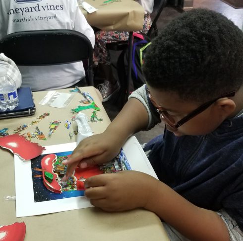 Young boy with glassed gluing his apple onto his Fazzino Pop Art project 