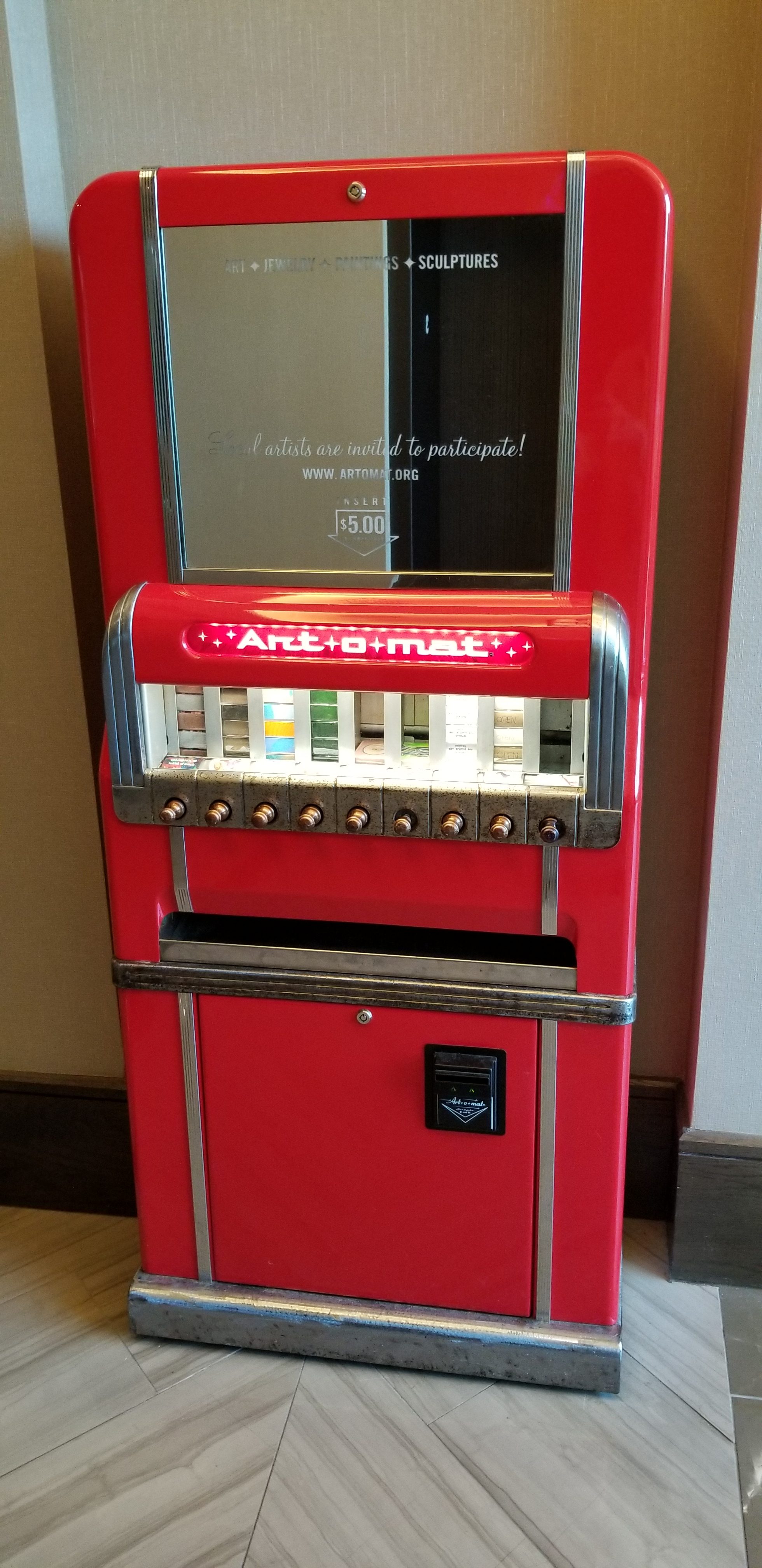 Red Art-O-Mat machine that looks like an old fashioned cigarette vending machine that sells art work 