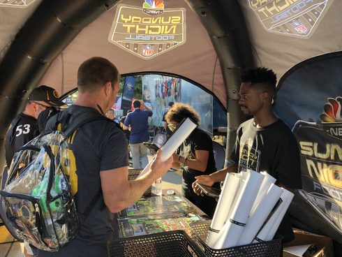 A fan at the Sunday Night Football booth picks up a poster by Fazzino