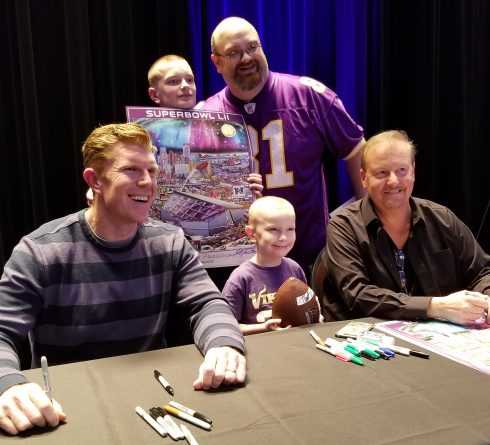 Super Bowl fans gathering around the Fazzino signing table are all smiles while the hold up their poster