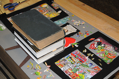 A stack of books on top of collage art work to help keep the images flat