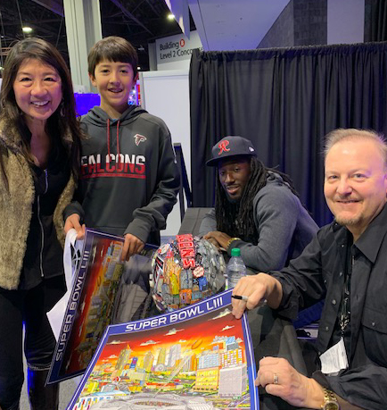 Charles Fazzino and Atlanta Falcons player Desmond Truffant sign posters for fans at the NFL Experience during Super Bowl LIII
