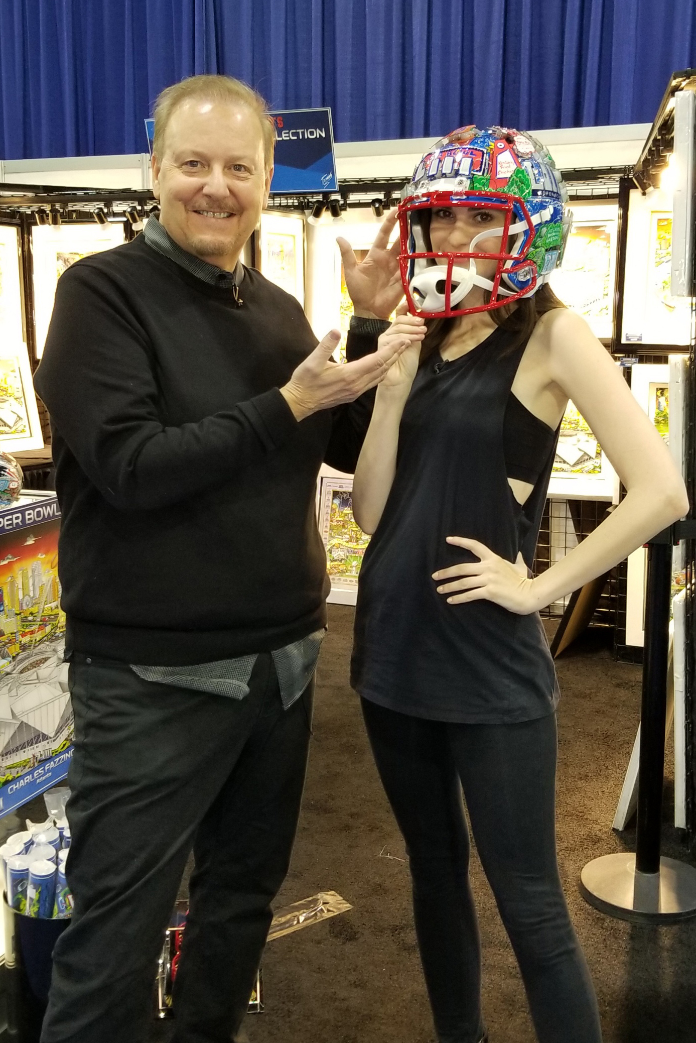 Charles Fazzino puts the Super Bowl LIII helmet on Kelleth Cuthbert's head as they stand in front of the NFL Experience booth