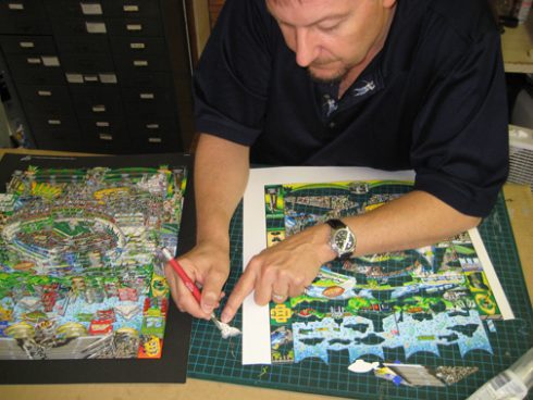 Charles Fazzino in the process of cutting out a cloud for one of his 3-D pop art pieces of a football stadium.