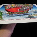 hand holding an 3D pop art print to show the new york city skyline and red apple with a nyc subway train going through it popping out from the page - 3D Pop Artist Charles Fazzino