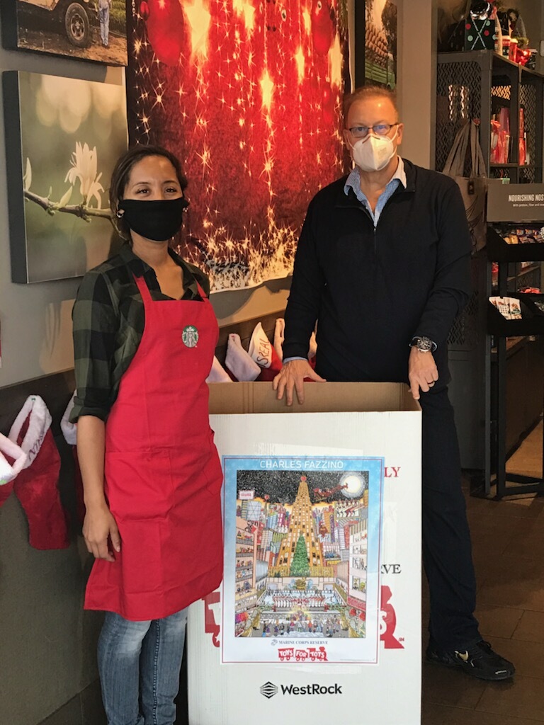 Fazzino standing next to a donation box adorning his Toys for Tots poster and Starbucks employee