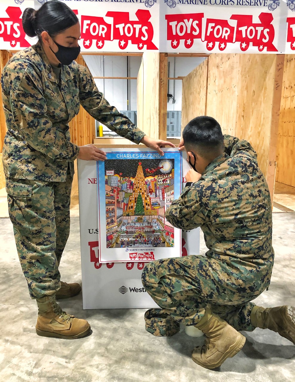 Two marines attaching Fazzino's Toys for Tots Official Poster to a donation box