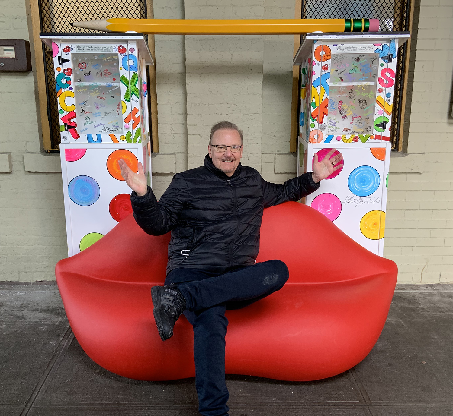 Charles Fazzino sitting on his new pop-up mini library installation at the New Rochelle train station 