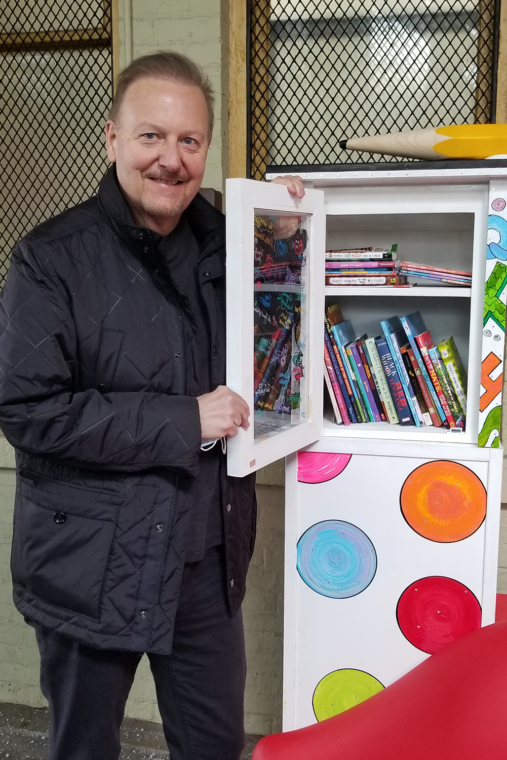 Charles Fazzino opening pop-up library kiosk door to show the wonderful amount of free books down at New Rochelle train station