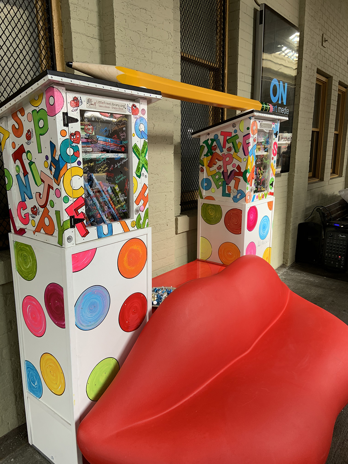 Pop-up library constructed of a pair of red lips, two mini library kiosks and a Ticonderoga pencil across the top. Charles Fazzino's pop art installation at New Rochelle train station