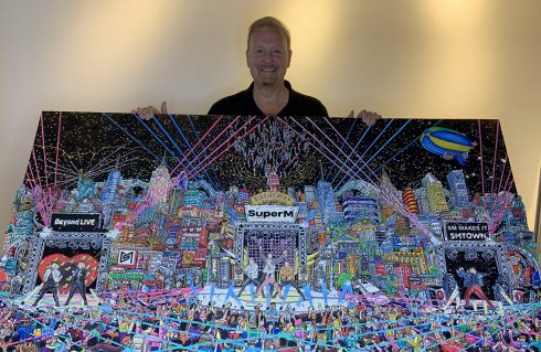 Charles Fazzino holding up 3d pop art commissioned piece for SMTOWN Museum, Seoul. Citycape of Korea with KPOP stars SUPERM front and center stage