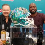 Charles Fazzino and Mathias Kiwanuka sitting on either side of a football helmet, decorated for Super Bowl 54