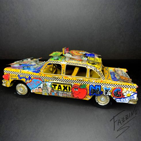 Side view of a yellow NYC taxi sculpture, with a city skyline, a smiling red apple, and NYC on the side