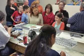 Small group of people watching two artists work in a studio