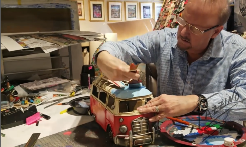 Artist Charles Fazzino paints the top of a VW bus sculpture blue