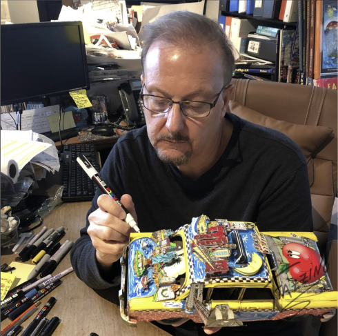 Artist Charles Fazzino uses a paint pen to add details to a yellow taxi cab art sculpture