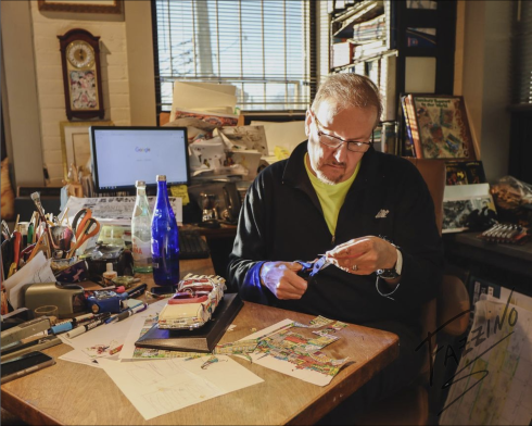 Artist Charles Fazzino sits behind a desk covered in art supplies as he works on a car sculpture