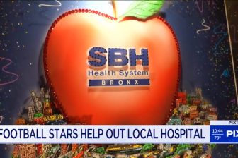A giant red apple with SBH Health System text across it and a NY cityscape in the background