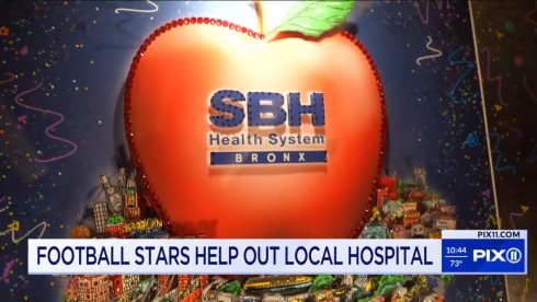 A giant red apple with SBH Health System text across it and a NY cityscape in the background
